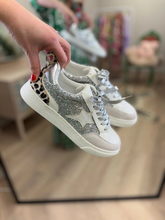 White sneakers with silver star designs held by a hand.