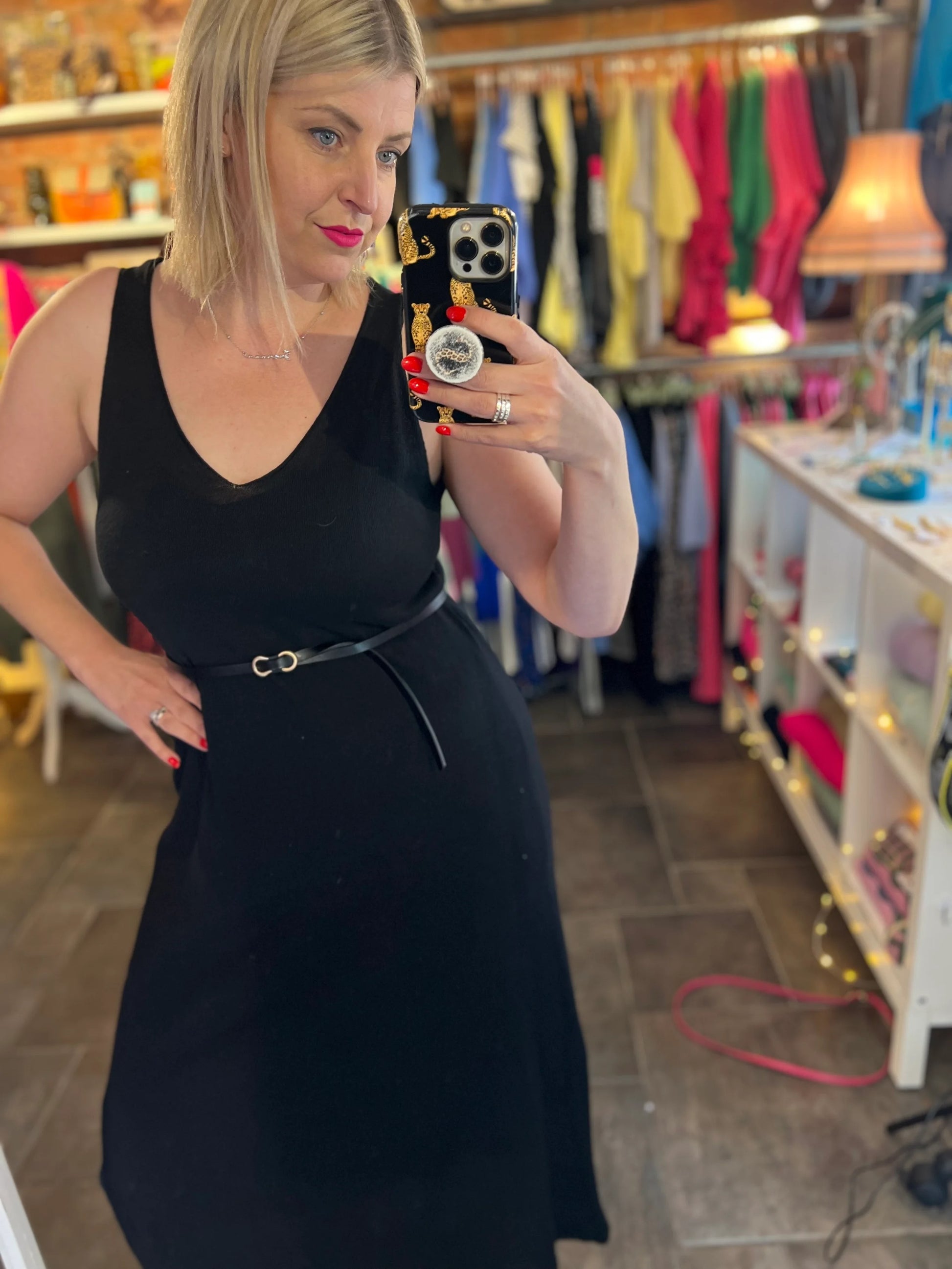 Woman taking a mirror selfie wearing a black dress in a clothing store.