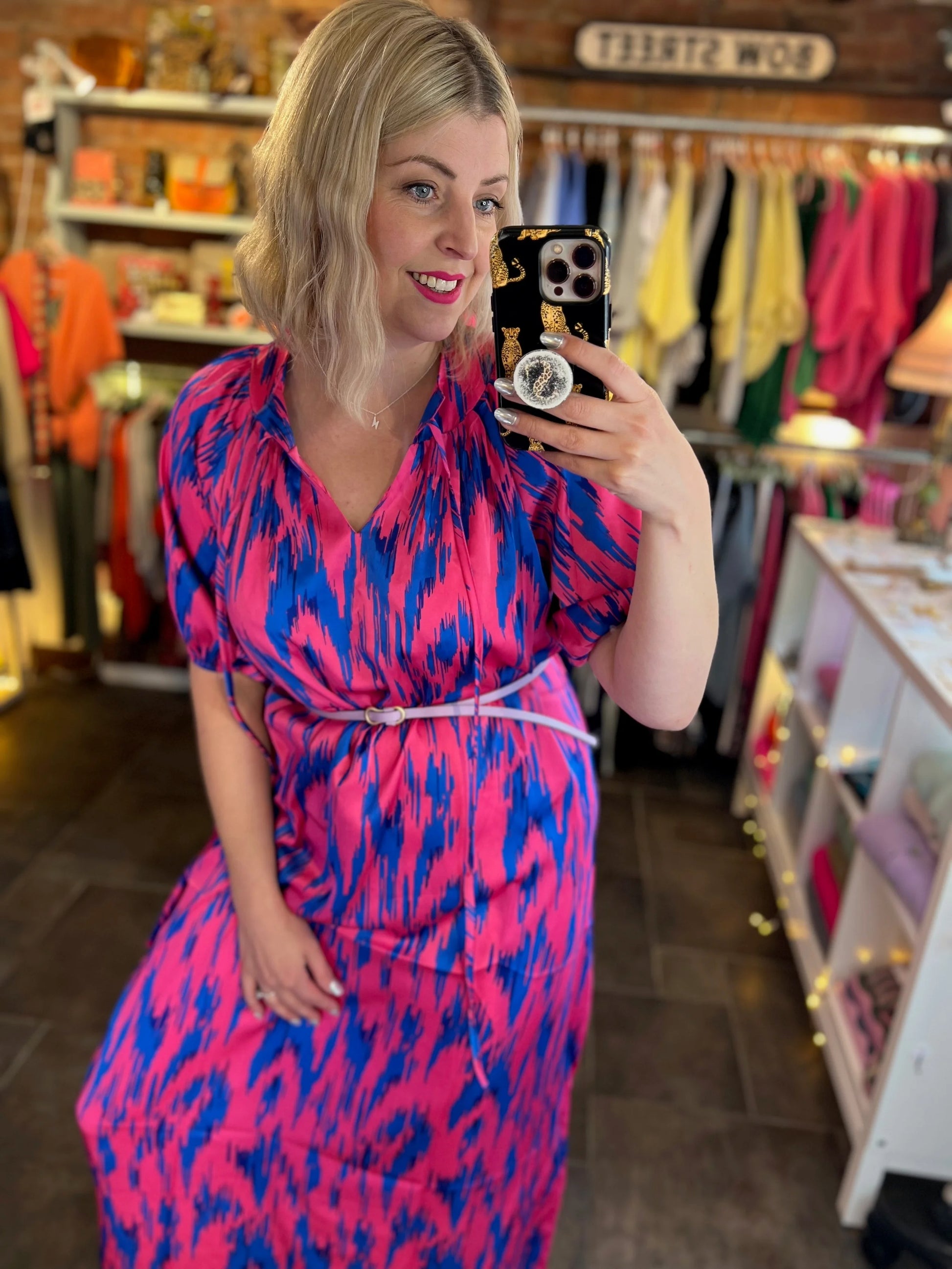 Woman taking a mirror selfie wearing a pink and blue dress in a store.