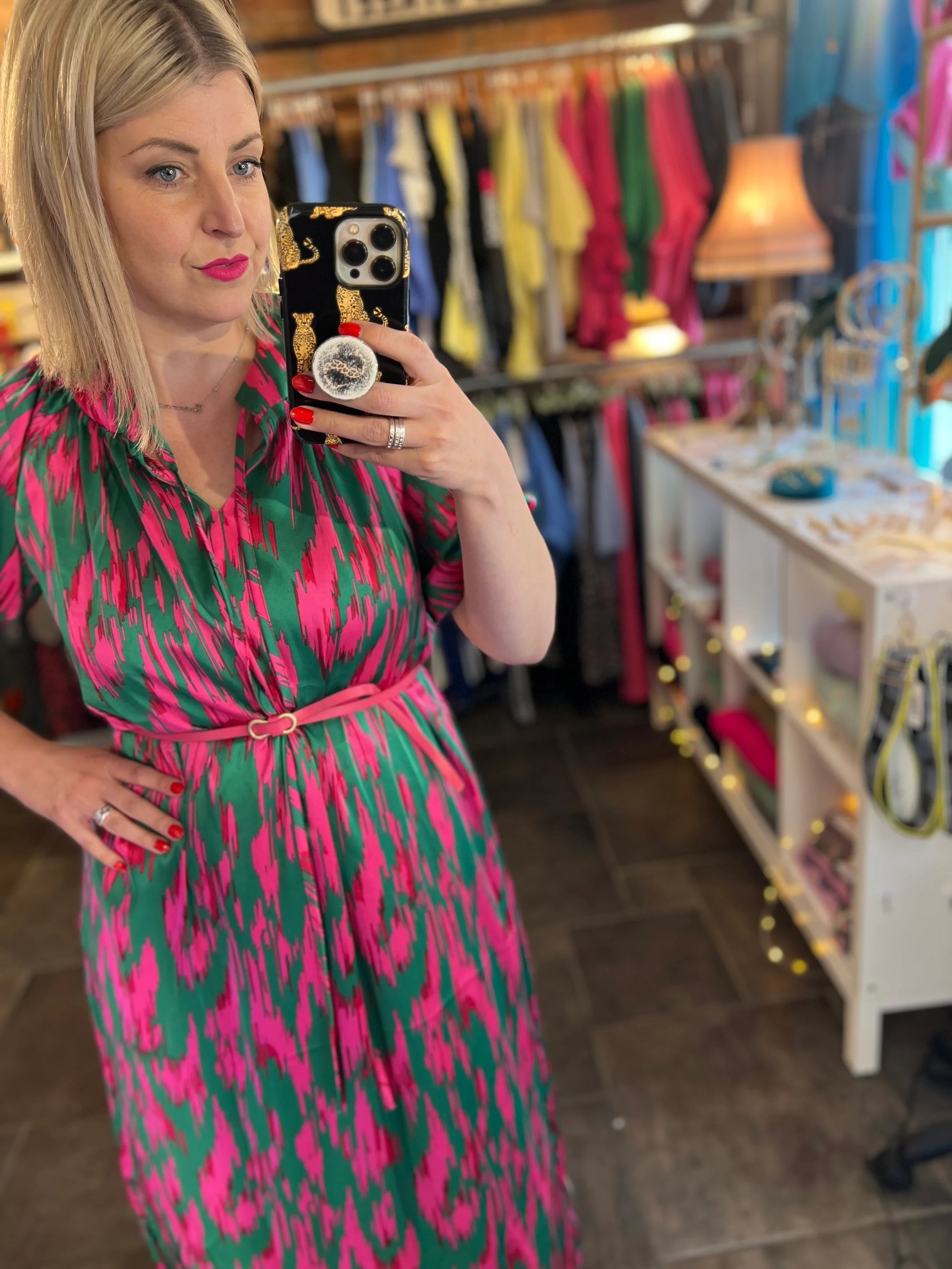 Woman taking a mirror selfie wearing a pink and green dress in a store.