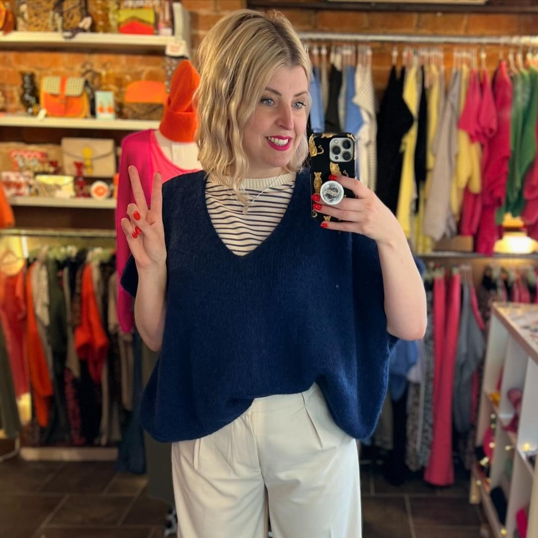 Woman taking a mirror selfie in a clothing store wearing a navy sweater and white pants.
