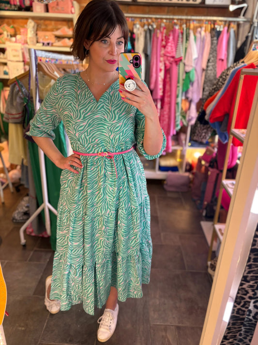 Person wearing a green patterned dress with a pink belt in a clothing store.