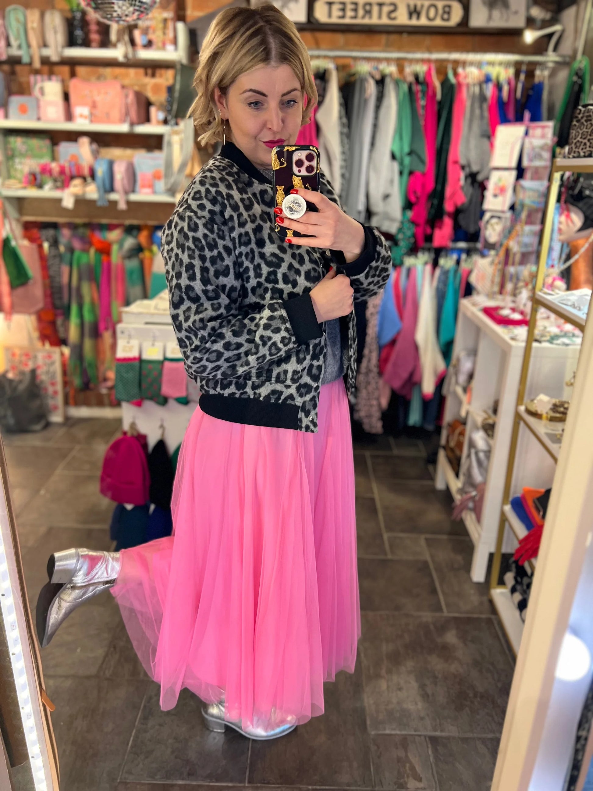 Woman taking a mirror selfie in a store wearing a leopard print sweater and pink tulle skirt.