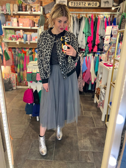 Woman taking a mirror selfie in a clothing store wearing a leopard print jacket, gray tulle skirt, and silver shoes.