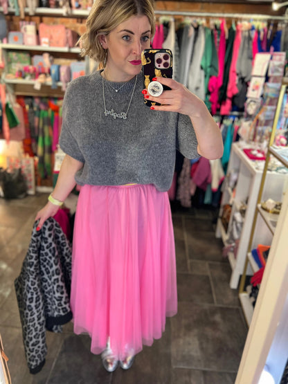 Person wearing a gray sweater and pink tulle skirt in a store setting.