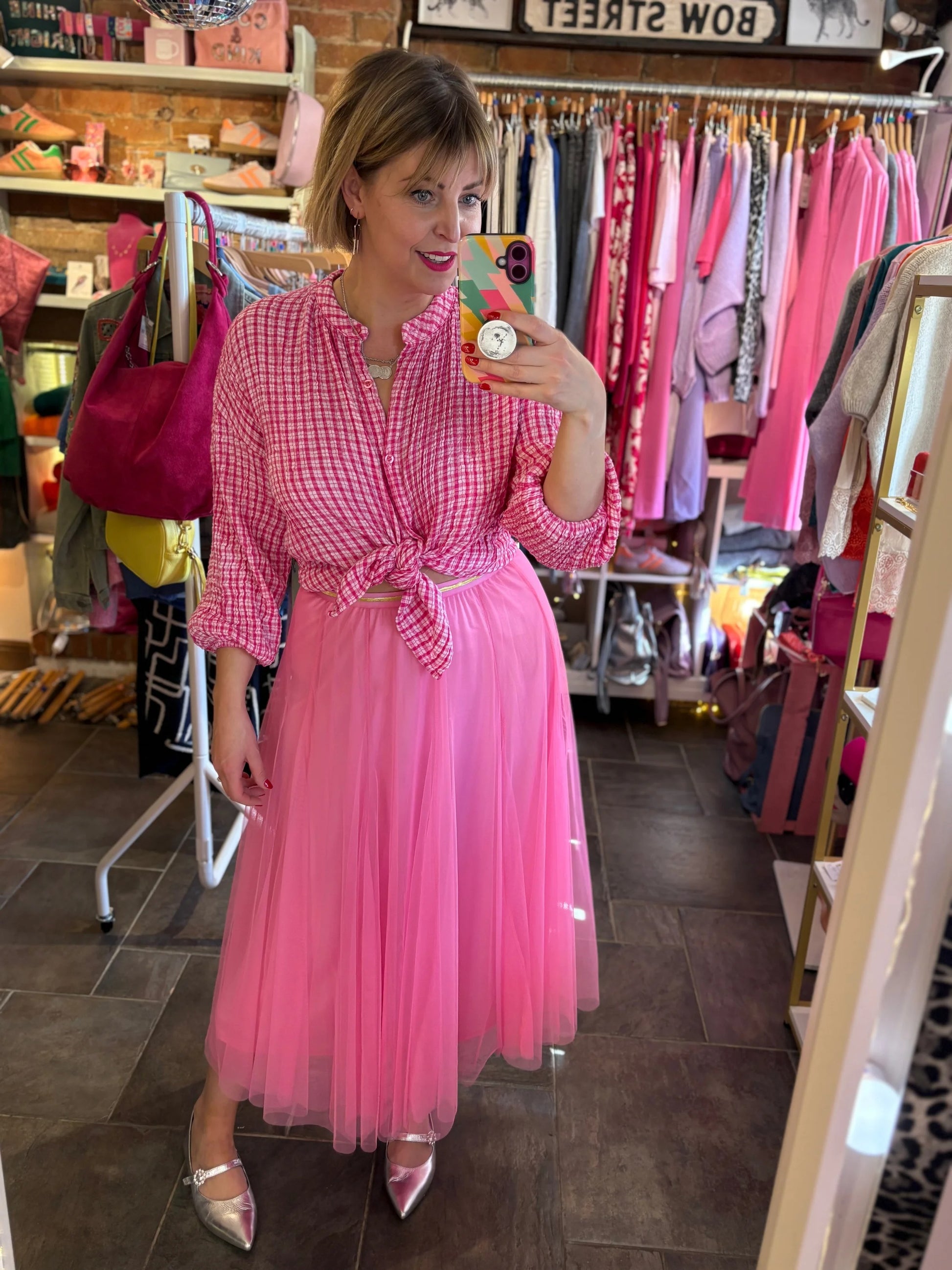 Woman in a pink dress taking a mirror selfie in a clothing store.