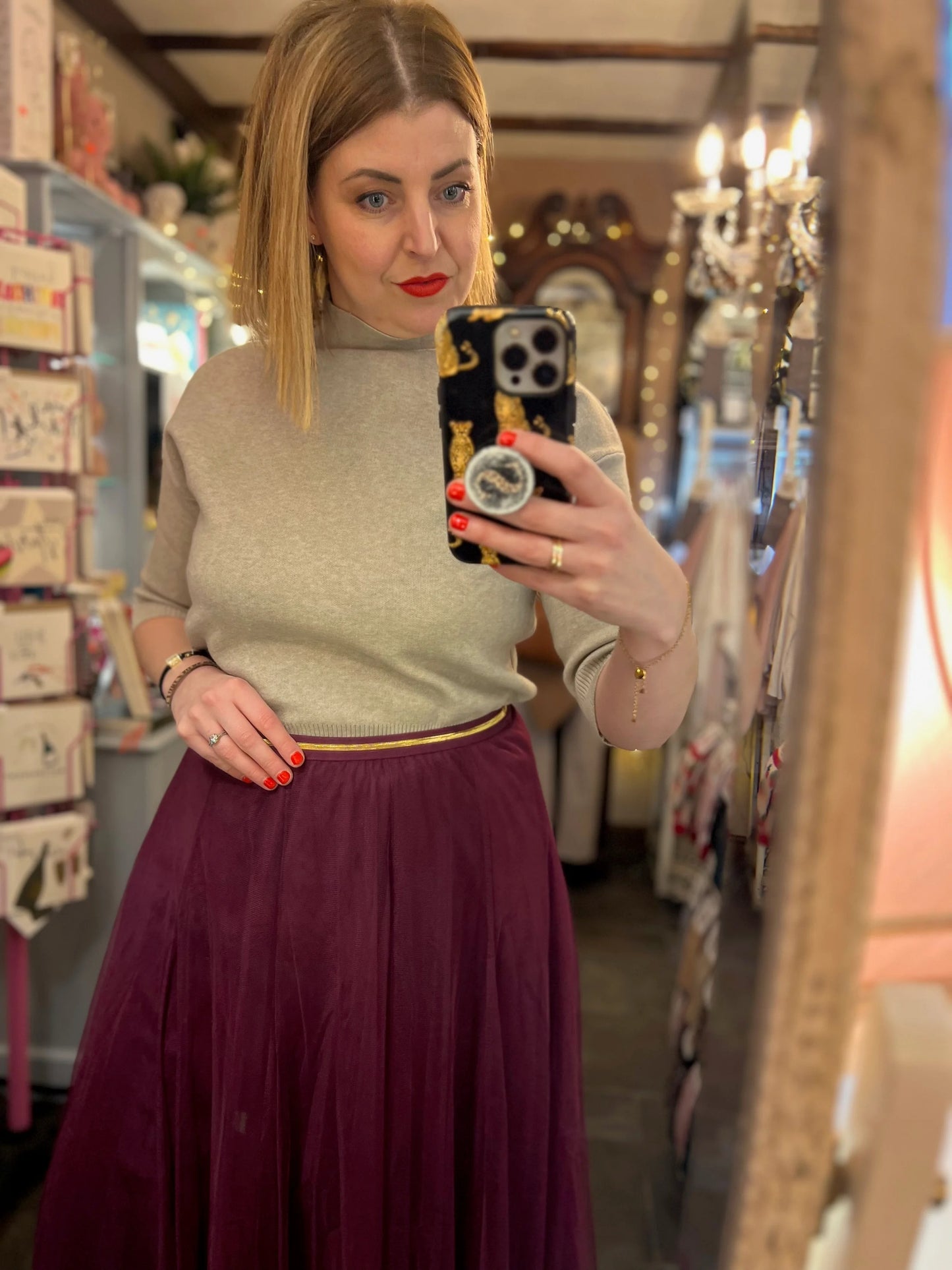 Woman taking a mirror selfie in a store with a phone case featuring a design.