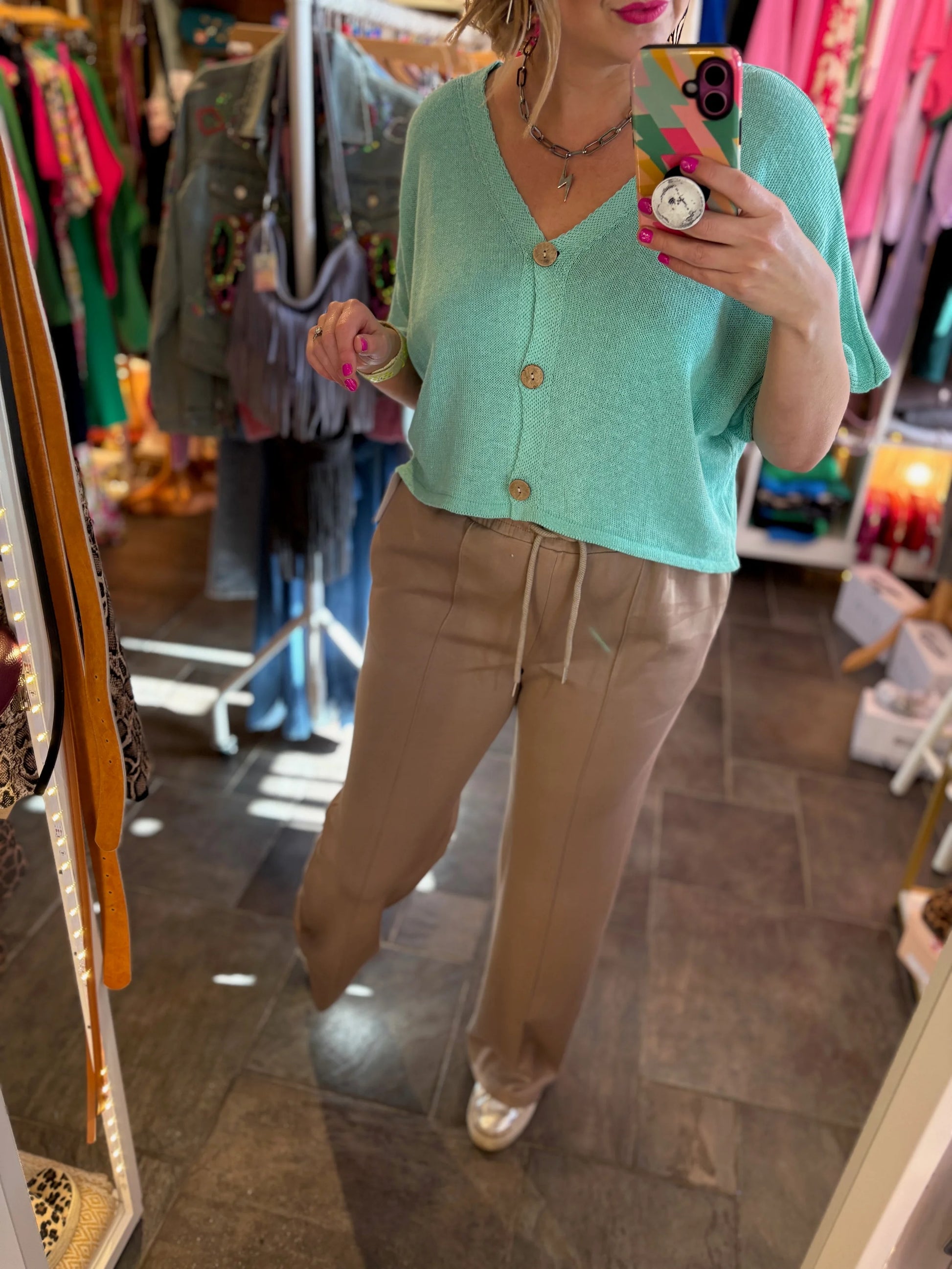Person wearing a green knitted top and beige pants in a clothing store.