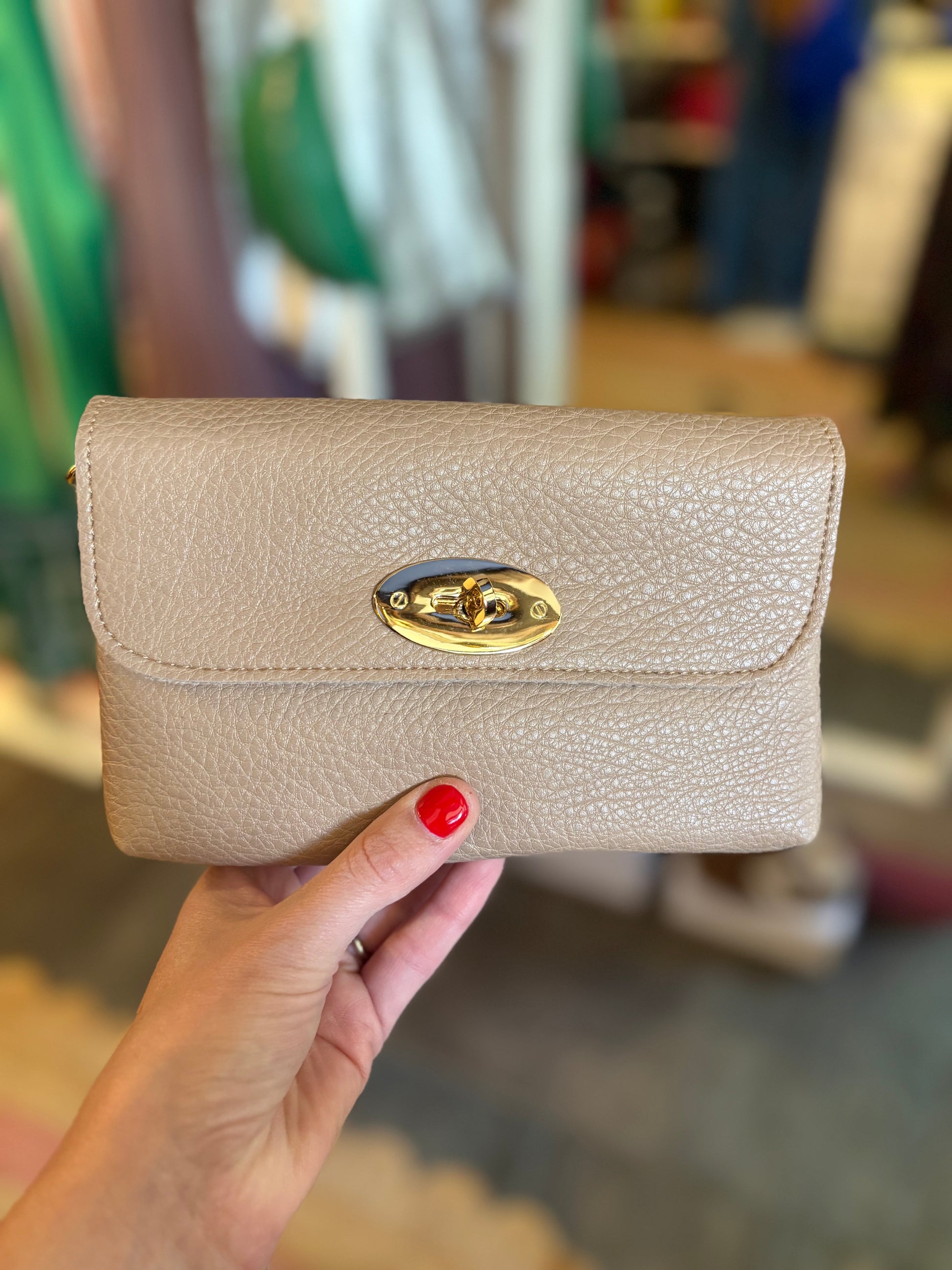 Beige wallet with gold clasp held by a hand in a blurred indoor setting