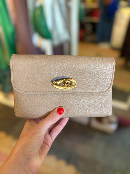 Beige wallet with gold clasp held by a hand in a blurred indoor setting