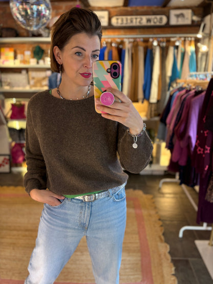 Woman taking a mirror selfie in a clothing store wearing a brown knit jumper and blue jeans.