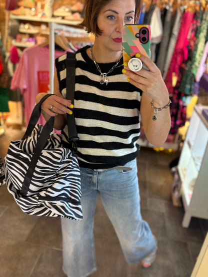 Person taking a mirror selfie wearing a striped top and jeans, holding a zebra-patterned bag in a store.
