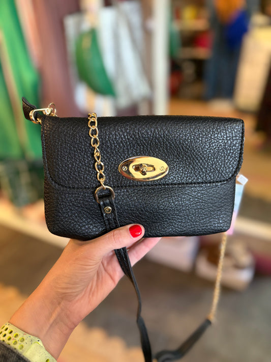 Black handbag with gold chain held by a person in an indoor setting