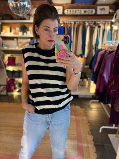 Person taking a mirror selfie wearing a black and white striped sleeveless knitted top and light blue jeans in a clothing store.