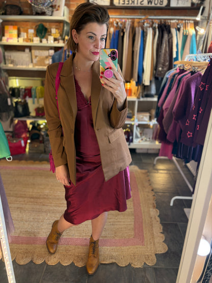 Woman taking a mirror selfie in a clothing store wearing a brown blazer and burgundy satin lace dress.