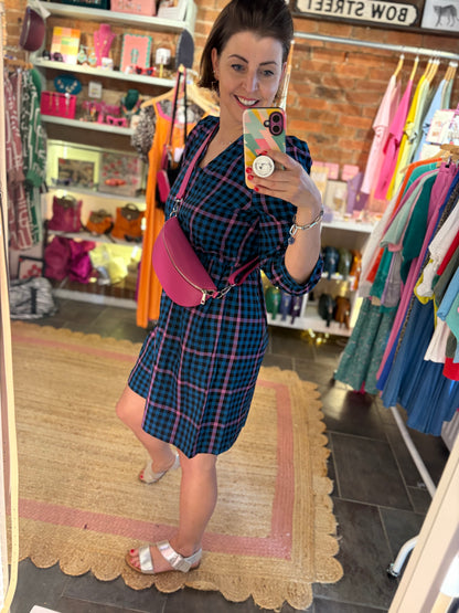 Woman taking a mirror selfie wearing a plaid dress and pink bag in a store.