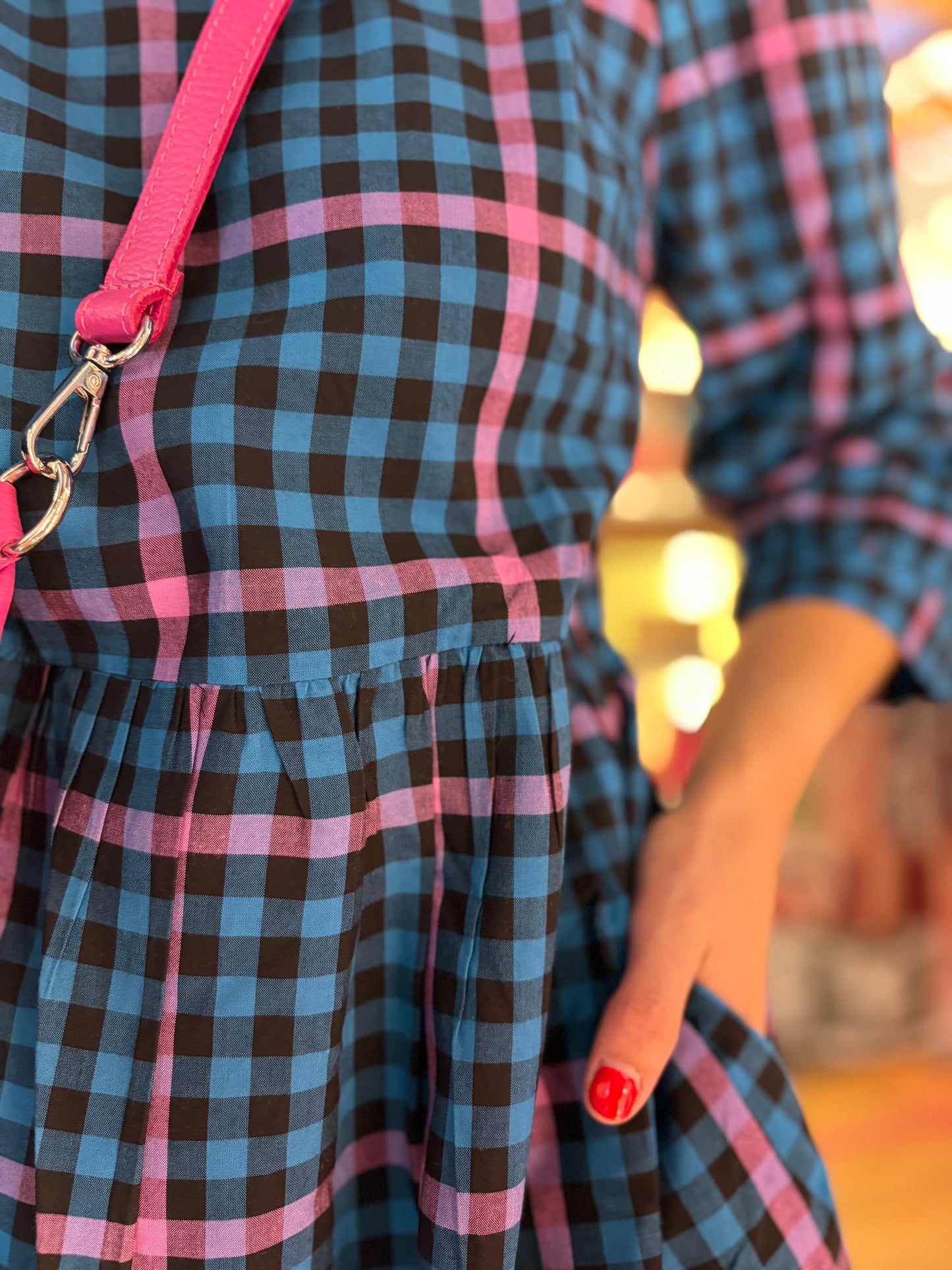 Close-up of a person wearing a blue and black checkered dress with pink straps.