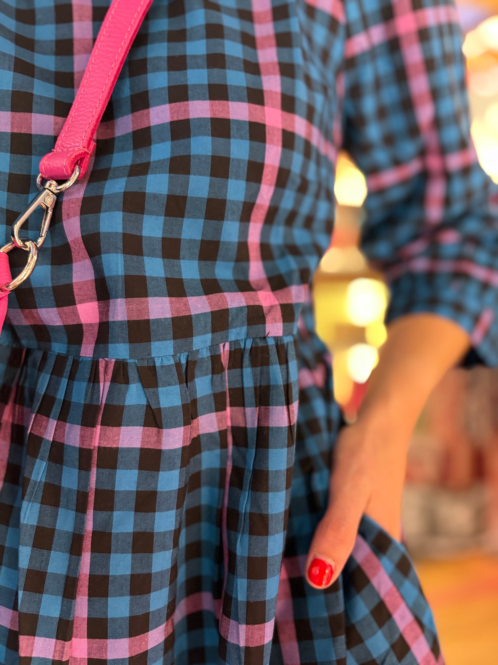 Close-up of a person wearing a blue and black checkered dress with pink straps.