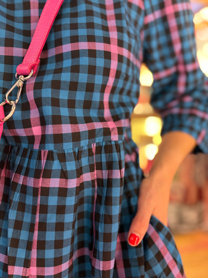 Close-up of a person wearing a blue and black checkered dress with pink straps.