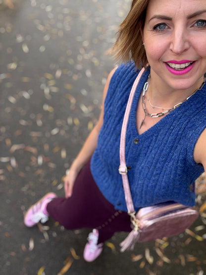 Woman in blue cable knit vest and pink trainers holding a pink bag 
