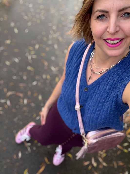 Woman in blue cable knit vest and pink trainers holding a pink bag 