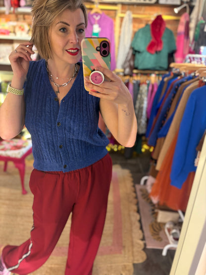 Woman taking a mirror selfie in a clothing store wearing a blue vest and red relaxed trousers