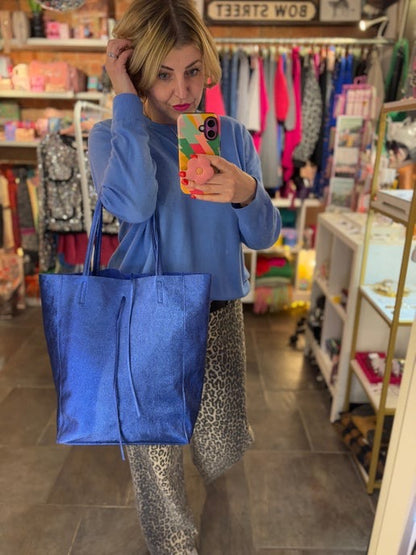 Woman taking a mirror selfie in a store holding a blue tote bag.