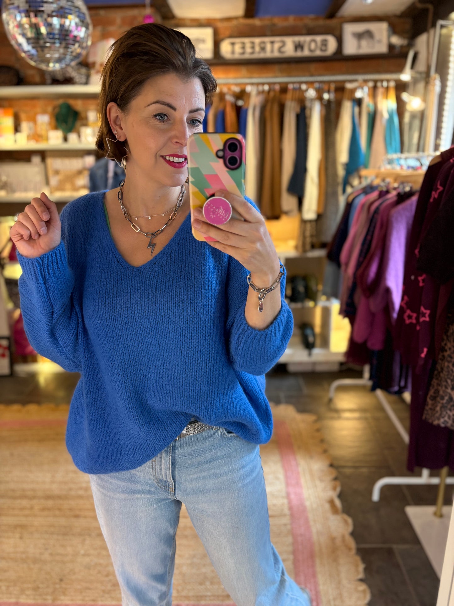 Woman taking a mirror selfie wearing a cobalt blue mohair knit sweater and light blue jeans in a clothing store.