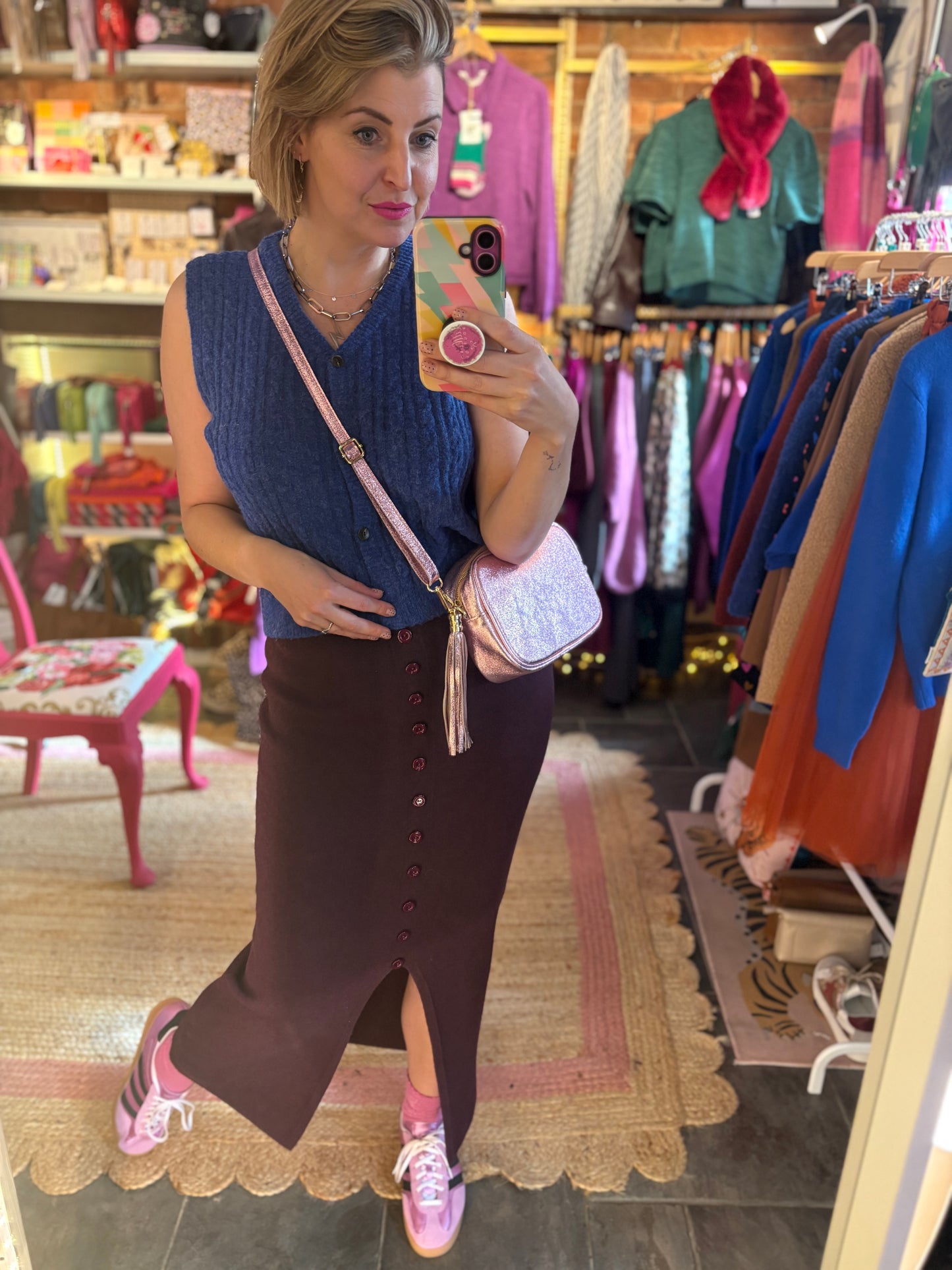 Woman taking a mirror selfie in a clothing store wearing a blue sleeveless top and burgundy skirt.