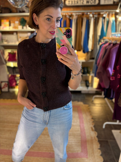 Woman taking a mirror selfie in a clothing store wearing a dark brown burgundy knit cardigan and light blue jeans.