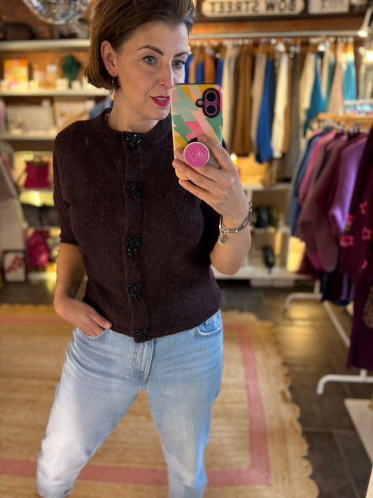 Woman taking a mirror selfie in a clothing store wearing a dark brown burgundy knit cardigan and light blue jeans.