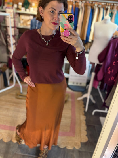 Woman taking a mirror selfie wearing a burgundy top and toffee satin slip skirt in a store setting.