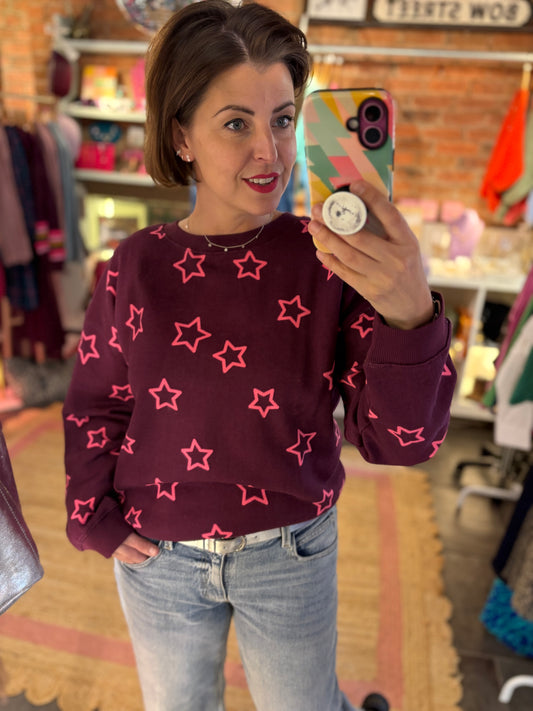 Woman taking a mirror selfie wearing a maroon sweater with pink star patterns in a store.