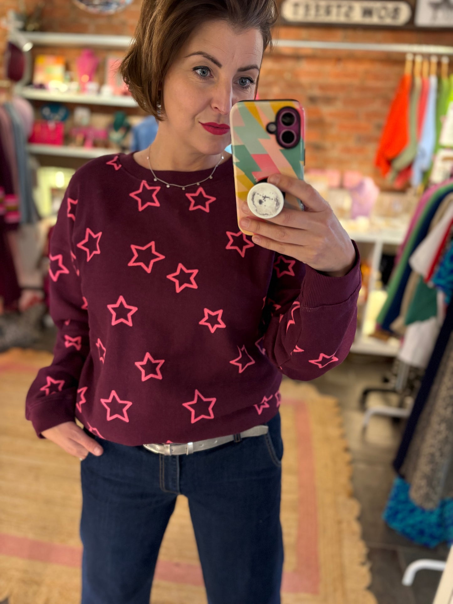 Person wearing a maroon sweater with pink star patterns in a store setting.