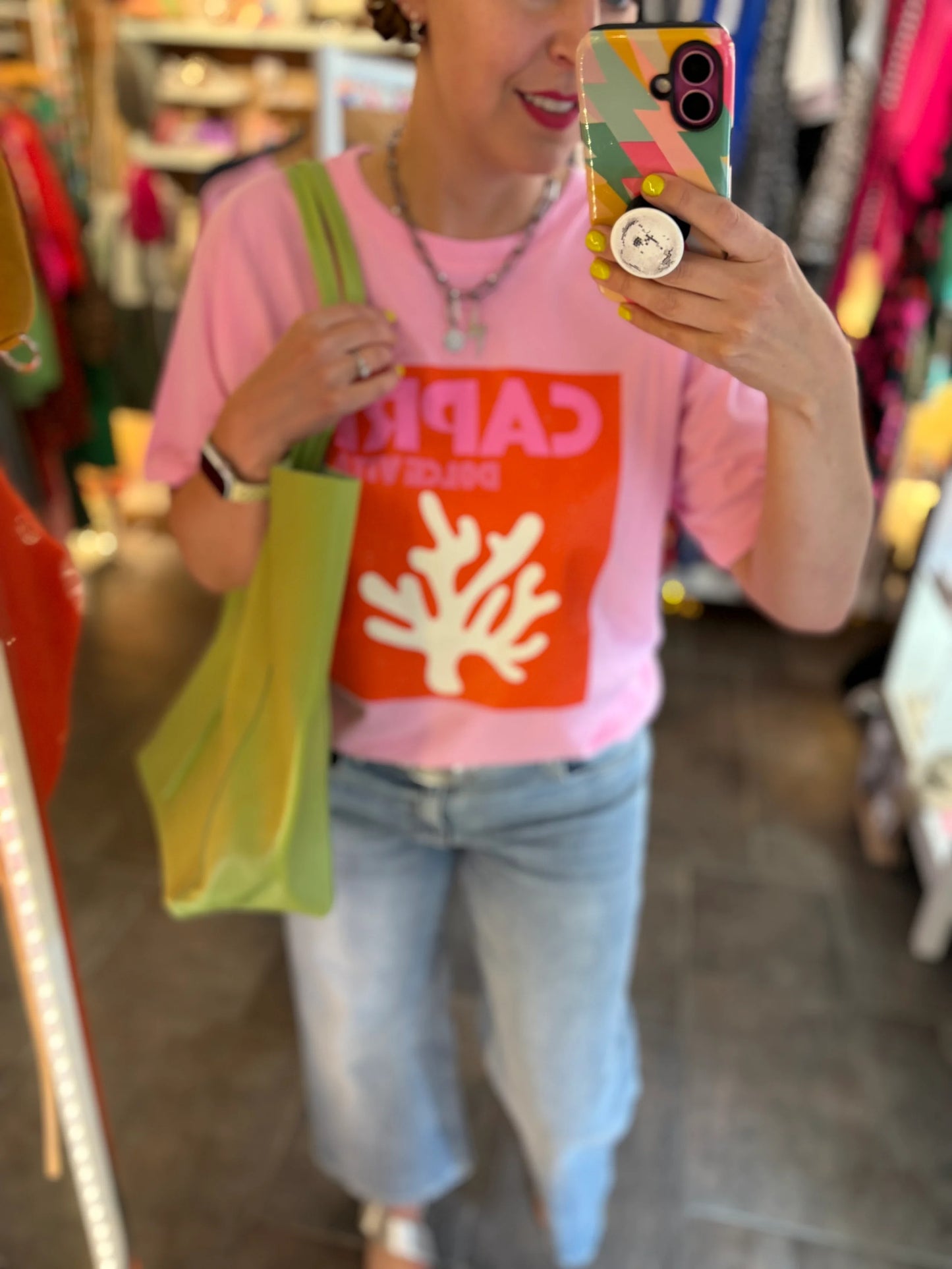 Person wearing a pink shirt with a colorful phone case and green bag in a store setting