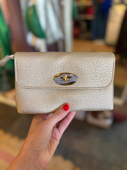 Hand holding a beige metallic  textured handbag with a gold clasp in an indoor setting.
