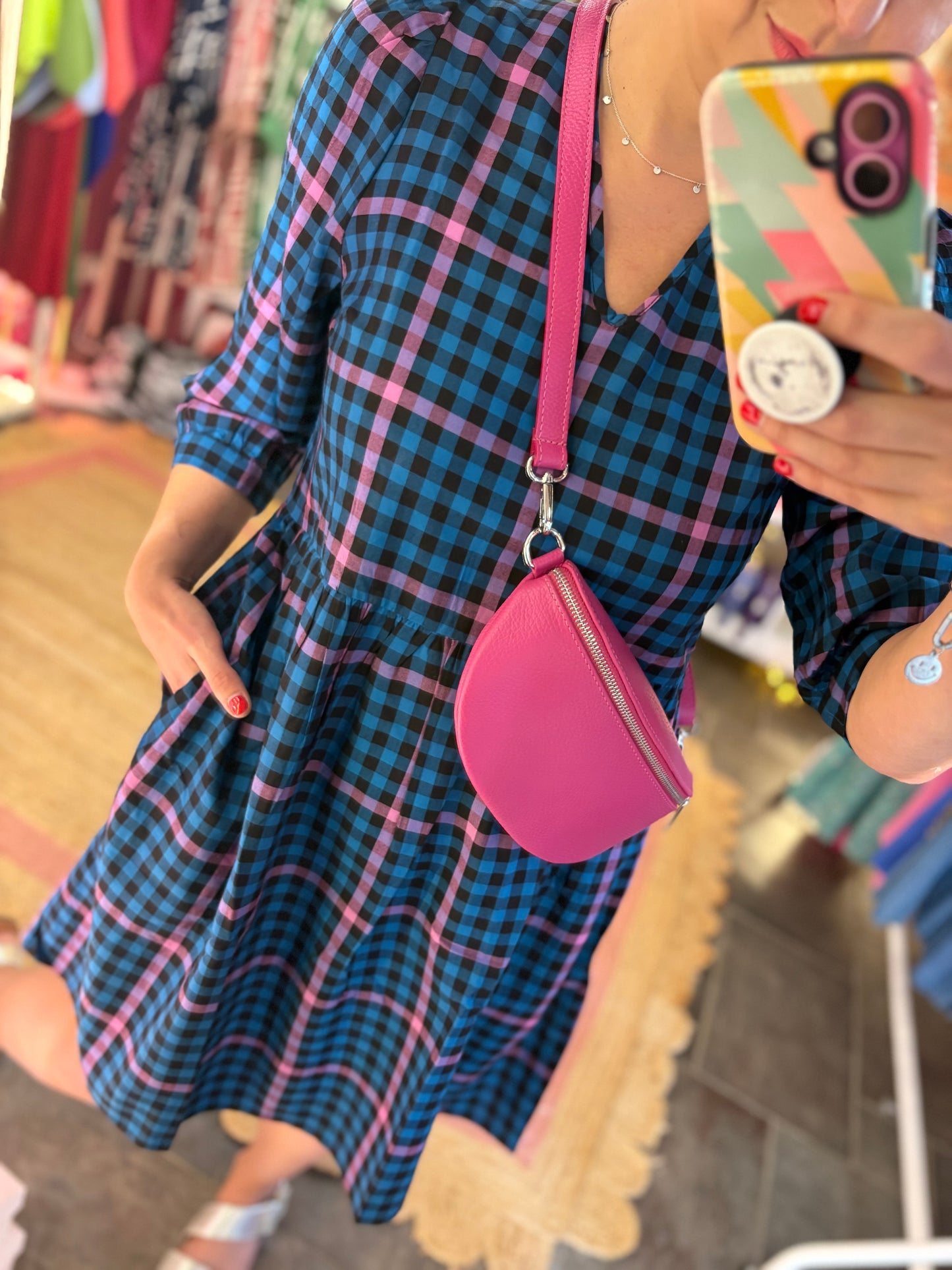 Person wearing a blue and pink checkered dress with a pink handbag, taking a mirror selfie.