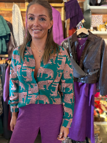 Woman wearing a cheetah print patterned blouse and purple pants in a clothing store.