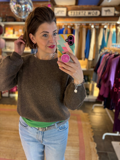 Woman taking a mirror selfie in a clothing store wearing a brown knit jumper  and blue jeans.