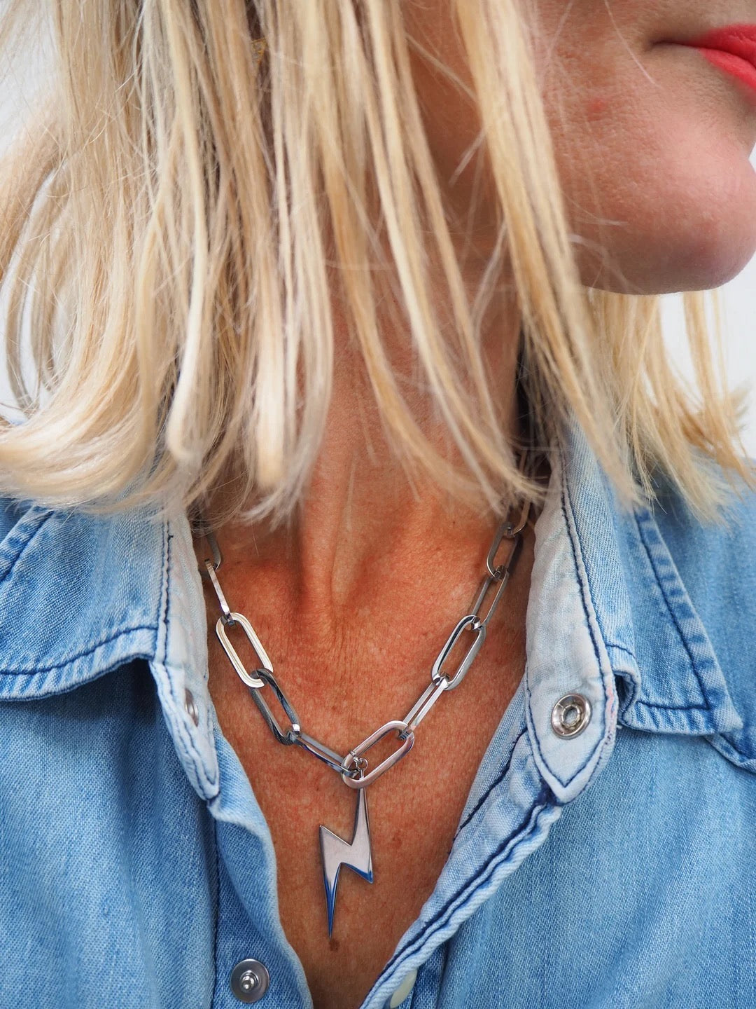 Person wearing a denim jacket with a necklace featuring a lightning bolt design.