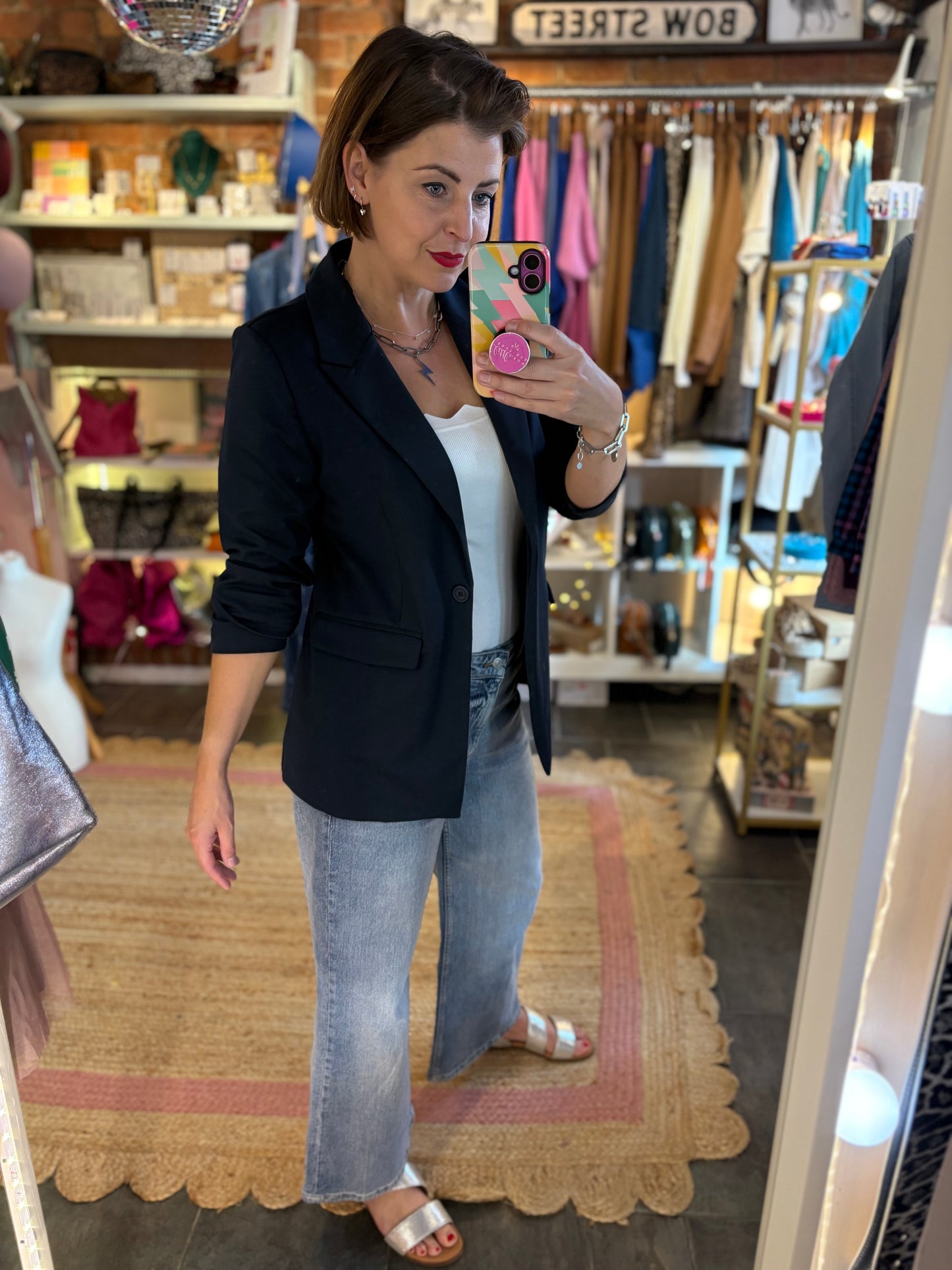 Woman taking a mirror selfie wearing a navy blue blazer and blue jeans in a store.