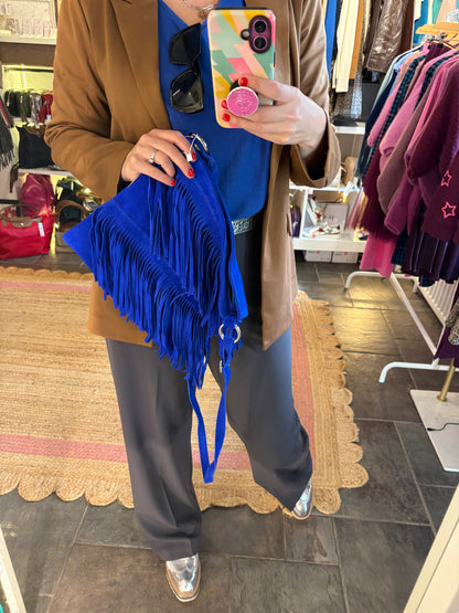Person holding a colorful phone case and blue suede fringed handbag in a store setting.