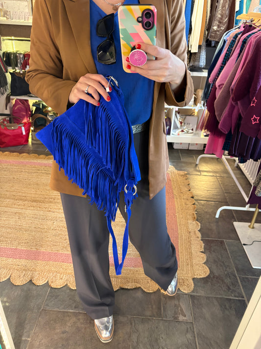 Person holding a colorful phone case and blue suede fringed handbag in a store setting.