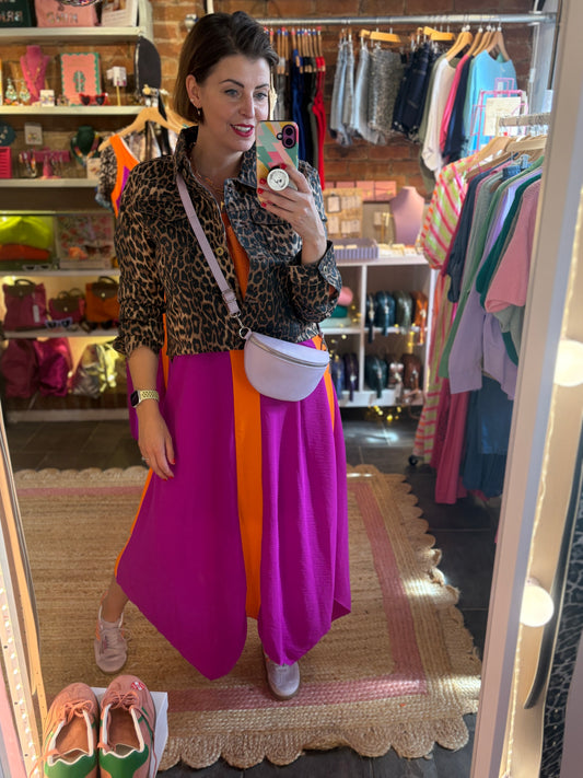 Woman taking a mirror selfie in a clothing store wearing a leopard print jacket over a magenta and orange dress.