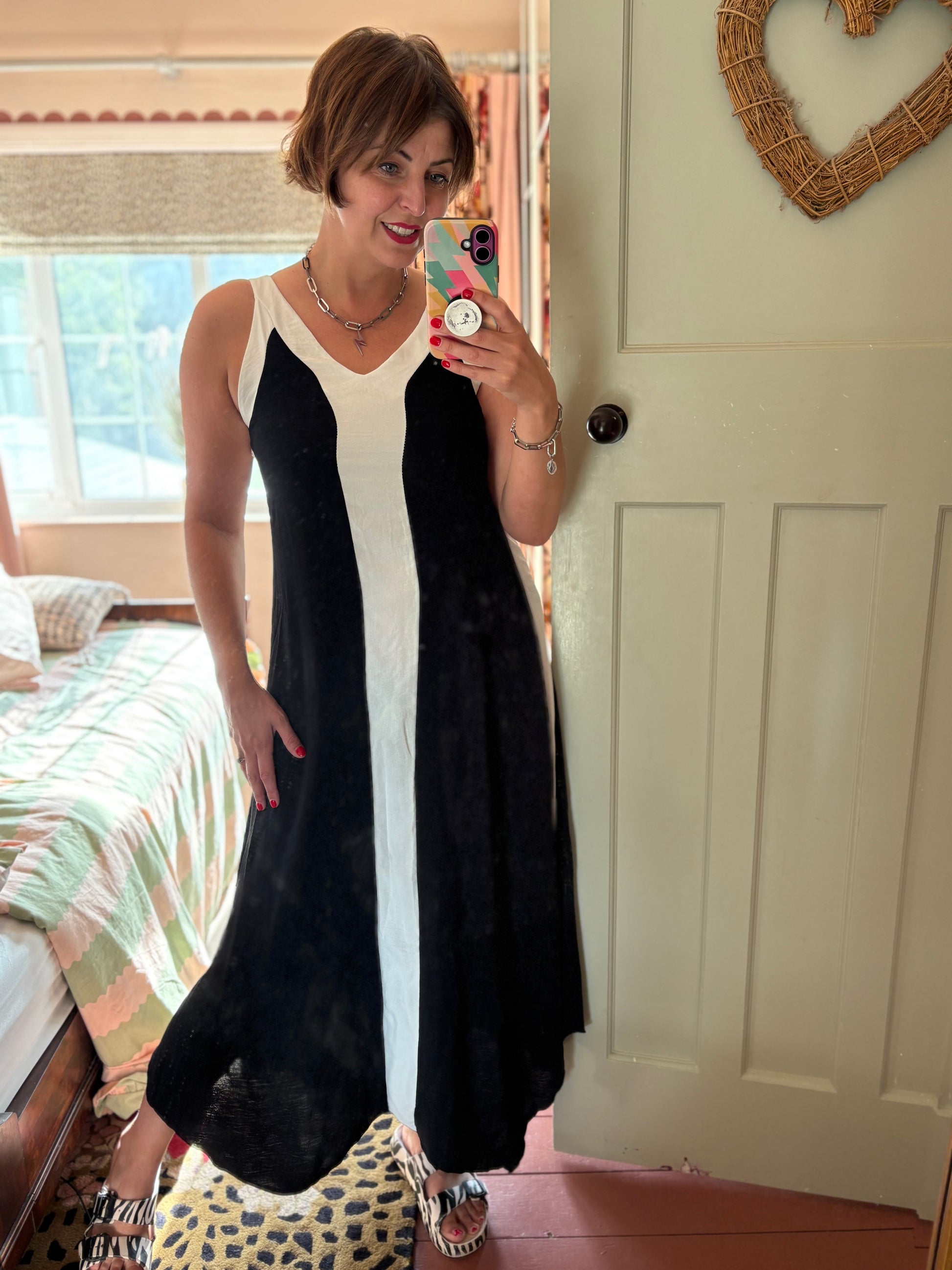 Woman taking a mirror selfie wearing a black and white dress in a bedroom.