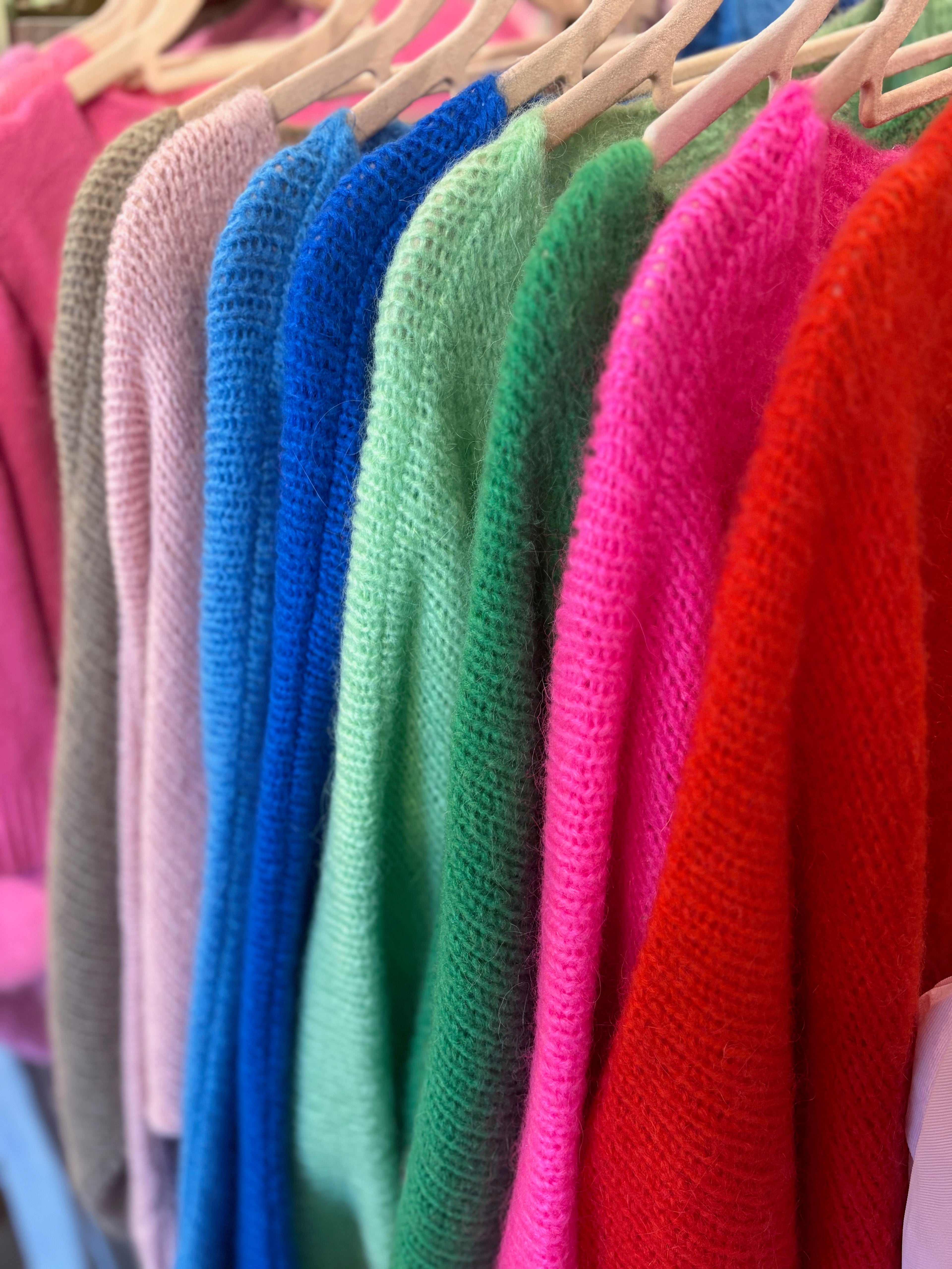 Row of colorful sweaters on hangers