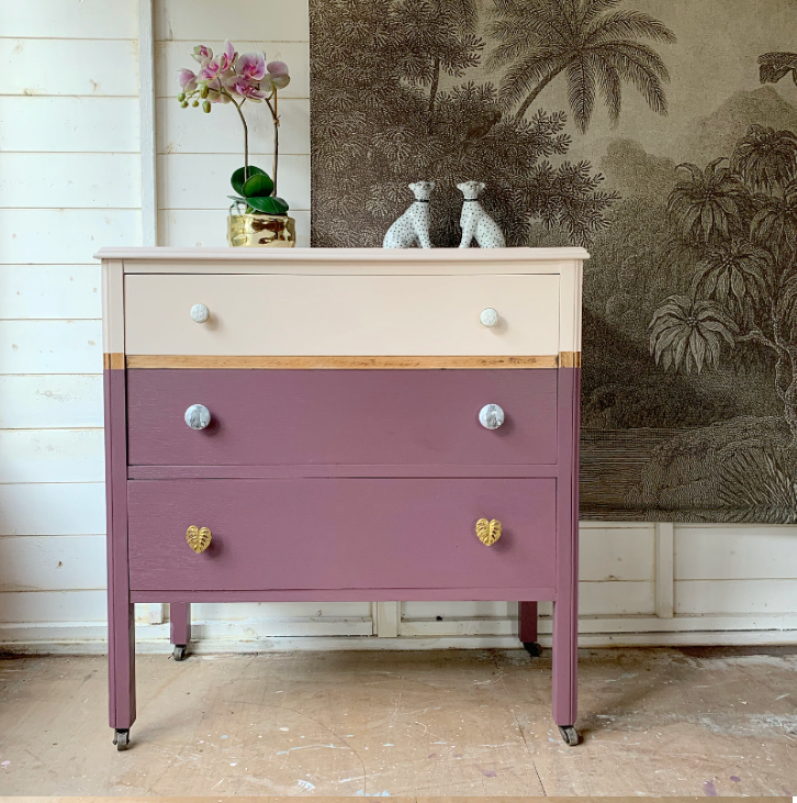 Two-toned dresser with gold accents in a room with decorative wallpaper.