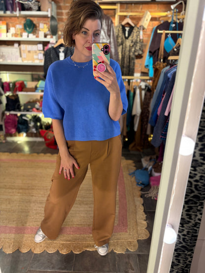 Person taking a mirror selfie wearing a blue top and brown pants in a clothing store.