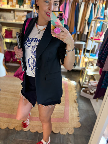 Woman taking a mirror selfie in a store, wearing a navy blazer over a graphic t-shirt.