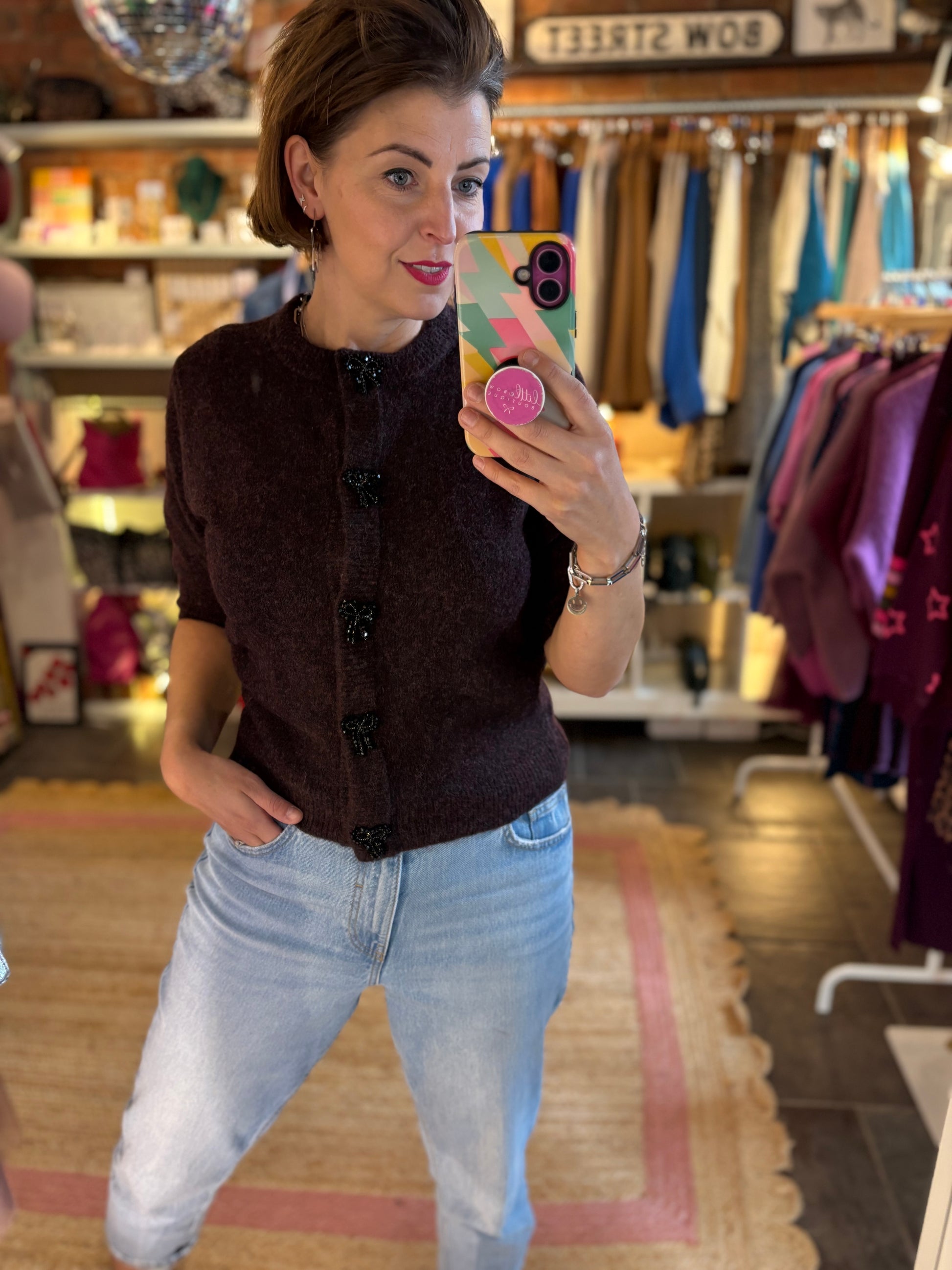 Woman taking a mirror selfie wearing a burgundy top and light blue jeans in a clothing store.